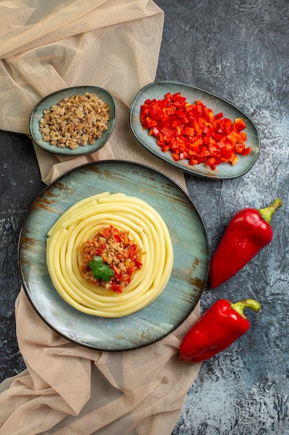 Бесплатное фото Вертикальный вид синей тарелки с вкусной пастой, подаваемой с помидорами и мясом на нарезанном полотенце коричневого цвета и целым перцем