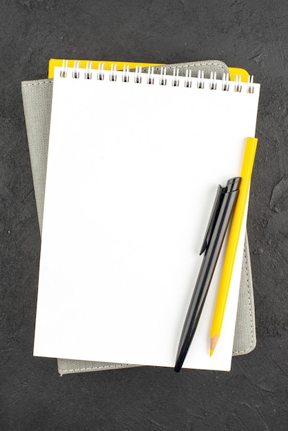 Бесплатное фото Вертикальный вид закрытых спиральных тетрадей и ручка-карандаш на черном
