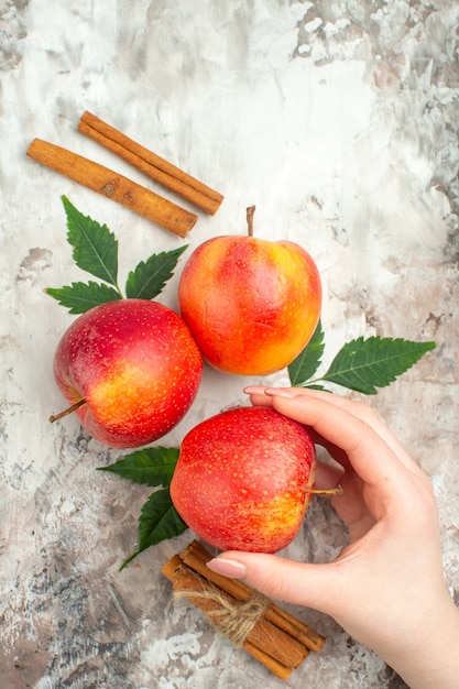 Вертикальный вид руки, держащей одно из свежих натуральных красных яблок и лаймов с корицей на смешанном цветном фоне