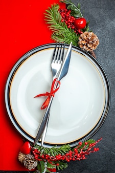 Вертикальный вид на рождественский фон с набором столовых приборов с красной лентой на аксессуарах для украшения тарелки еловых веток на красной салфетке