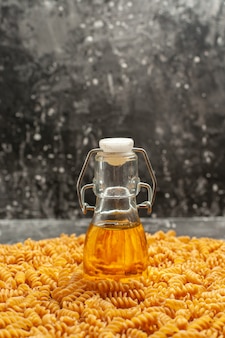 Vista verticale della bottiglia di olio in piedi su pasta italiana cruda allineata in un cerchio su sfondo grigio