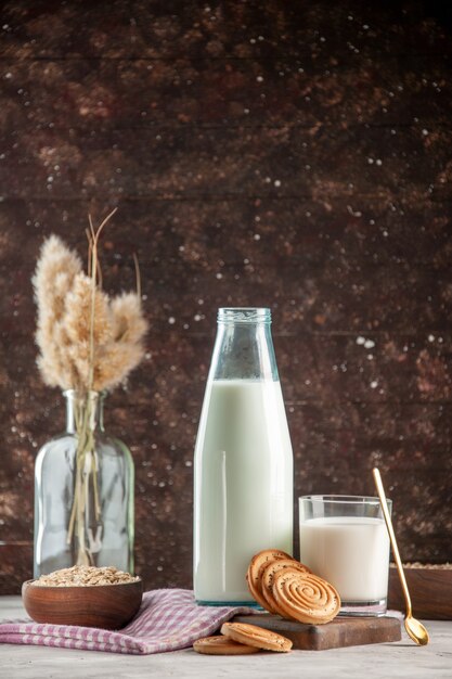 Vertical view of open glass bottle and cup filled with milk cookies oats in brown pot on purple stripped towel on wooden cutting board