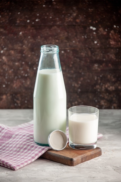 Vertical view of open glass bottle and cup filled with milk on purple stripped towel on wooden cutting board