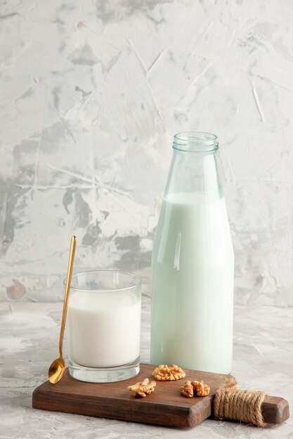 Vertical view of open glass bottle and cup filled with milk spoon and walnut on ice background