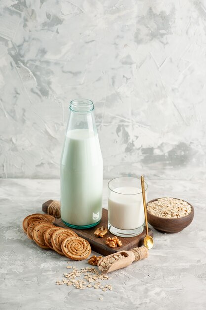 Vertical view of open glass bottle cup filled with milk spoon and walnut oats in brown pot cookies on ice background