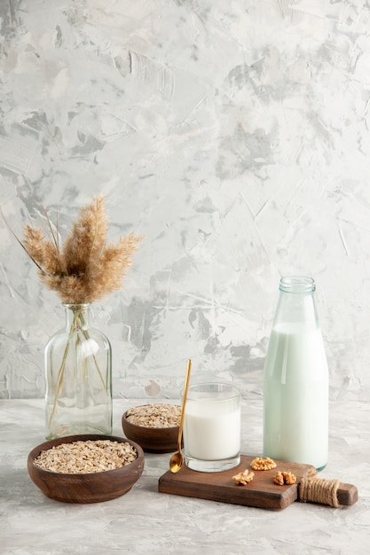 Vertical view of open glass bottle cup filled with milk spoon and walnut oats in brown pot on ice wall