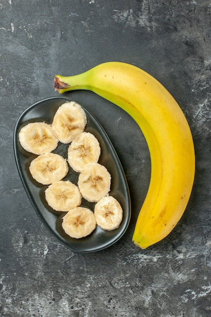 Вертикальный вид источника органического питания свежий банан, нарезанный и целиком на темном фоне