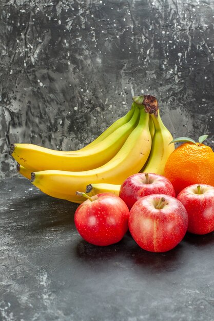 어두운 배경에 유기농 영양 공급원 신선한 바나나 번들과 빨간 사과 오렌지의 수직 보기