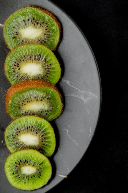 Free photo vertical view of plate of sliced kiwis on black surface