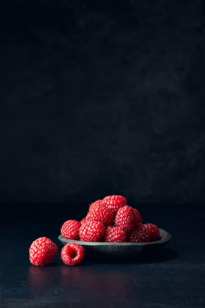 Vertical view of raspberries in a plate on a black surface