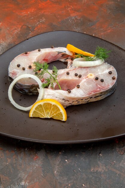 Vertical view of raw fishes and pepper lemon slices onion on a black plate on mix color surface