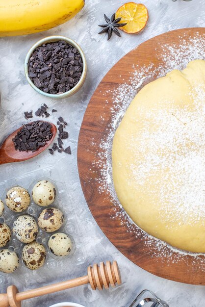 Vertical view of raw pastry flour on round board cookies fresh fruits eggs banana wooden spoon on stained white background