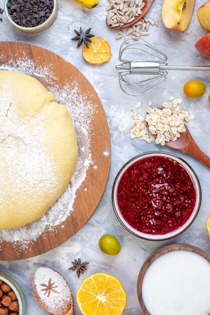 Vertical view of raw pastry flour on round board cookies fresh fruits on stained white background