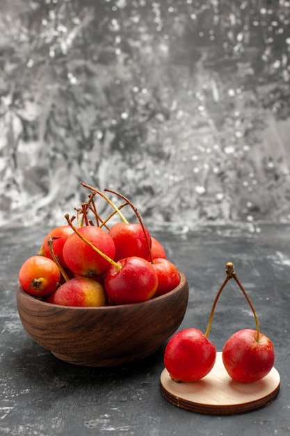 Vertical view of red cheries in a brown bowl and on small wooden tray on gray