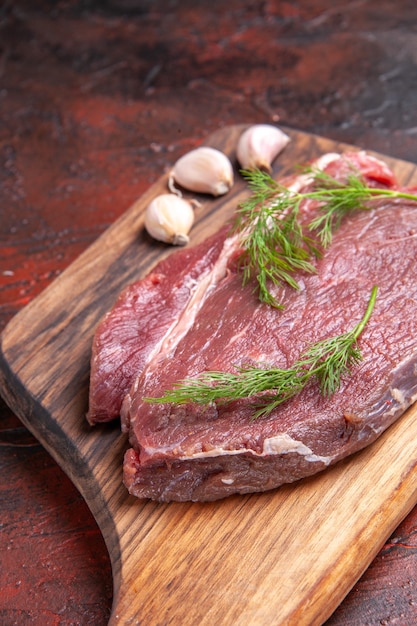 Vertical view of red meat on wooden cutting board and garlic green on dark background