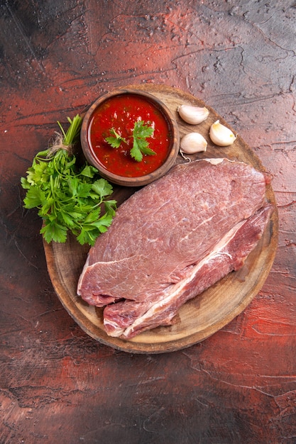 Vertical view of red meat on wooden tray and garlic green ketchup on dark background