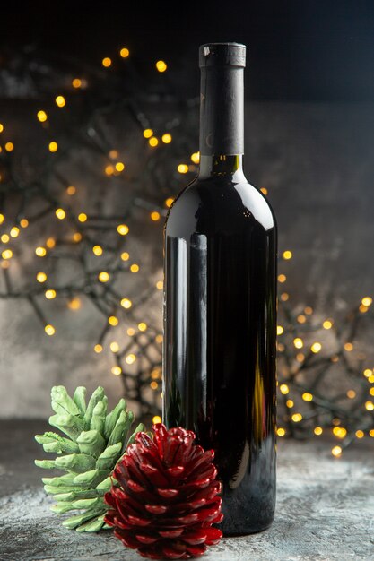 Вертикальный вид бутылки красного вина для празднования и двух хвойных шишек на темном фоне