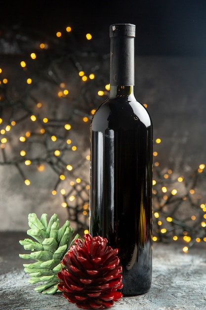 Vertical view of red wine bottle for celebration and two conifer cones on dark background