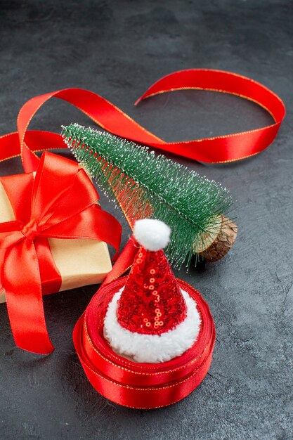 Vertical view of santa claus hat on a roll of ribbon and beautiful gift christmas tree on dark background