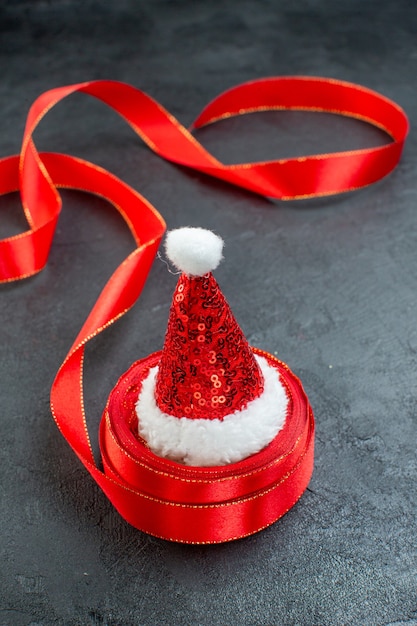 Vertical view of santa claus hat on a roll of ribbon on the right side on dark background