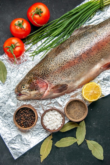 Vertical view of scales removed fresh fish tomatoes and different spices on dark color background