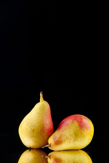 Vertical view of single whole ripe yellow with red pears lying on black background