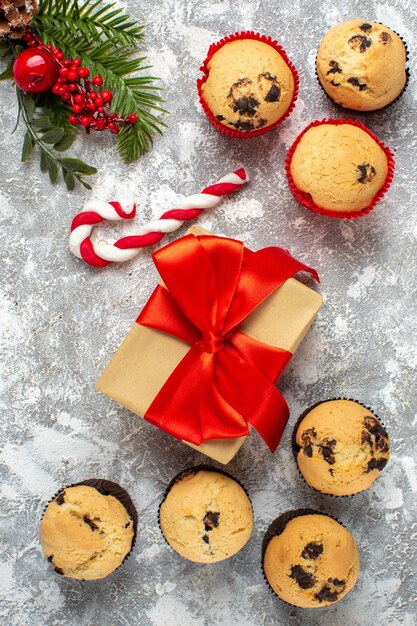 Vertical view of small cupcakes Christmas gifts with red ribbon and candy fir branches on ice surface