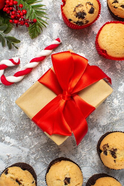 Vertical view of small cupcakes Christmas gifts with red ribbon and candy fir branches on ice table