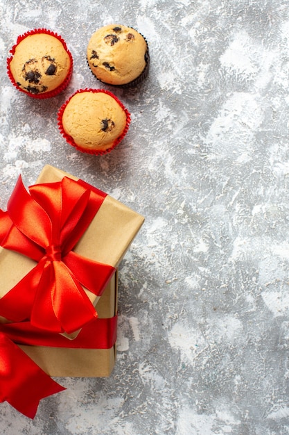 小さなカップケーキの垂直方向のビュー氷の表面に赤いリボンのクリスマスプレゼント
