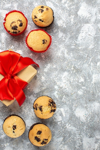 Vertical view of small cupcakes Christmas gifts with red ribbon on the right side on ice surface