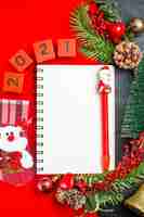 Free photo vertical view of spiral notebook decoration accessories fir branches xsmas sock numbers on a red napkin and christmas tree on dark background