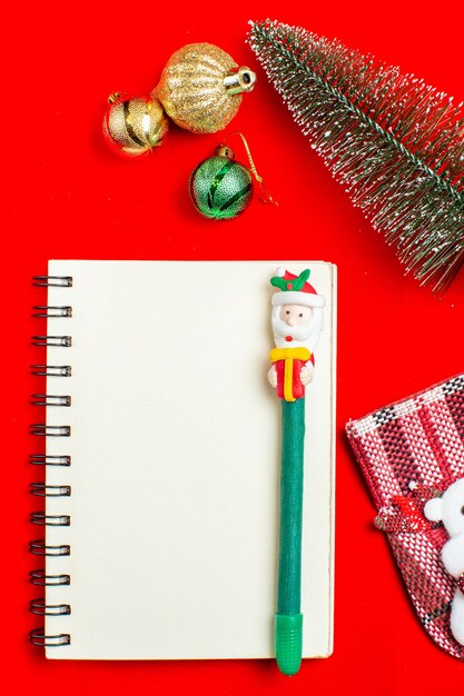 Vertical view of spiral notebook with pen christmas tree decoration accessories on red background