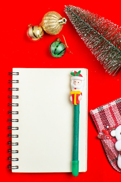 Vertical view of spiral notebook with pen christmas tree decoration accessories on red background