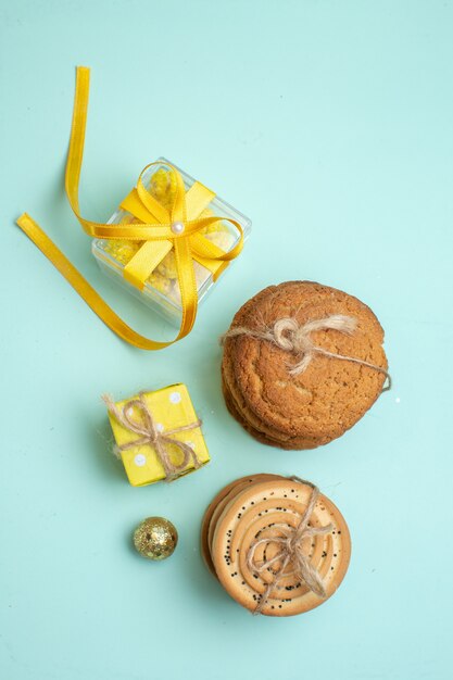 Vertical view of stacked various delicious cookies and beautiful yellow gift boxes on pastel green background