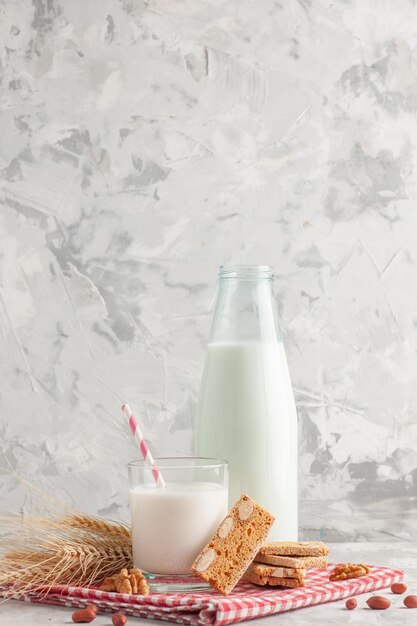Вертикальный вид конфеты в форме палочки в стеклянной бутылке, наполненной молоком и выпечкой, арахисом на красном полосатом полотенце на сером фоне
