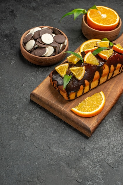 Vertical view of tasty cakes cut lemons with biscuits on cutting board on dark table