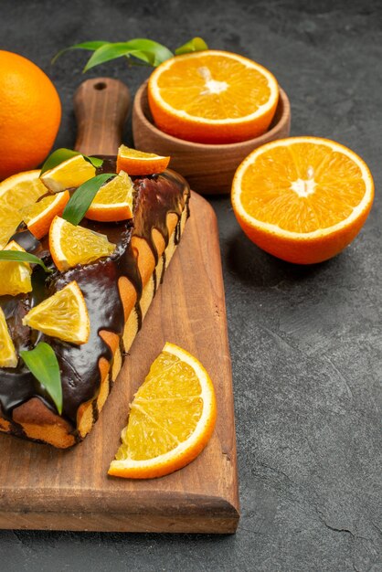 Vertical view of tasty cakes whole and cut lemons on cutting board on black table