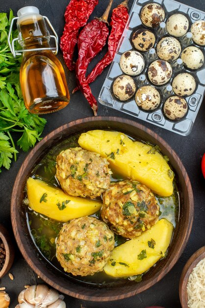 Vertical view of tasty meatball meal fresh vegetables eggs green fallen oil bottle on black background