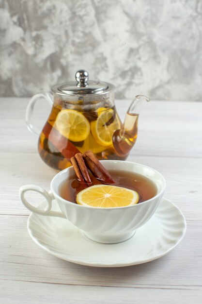 Vertical view of tea time with mixed herbal tea with lemon in a glass pot and a cup on white table