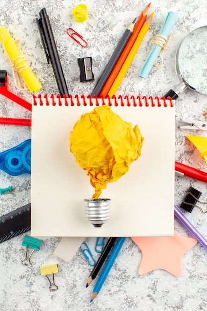 Vertical view of time torn balloon on spiral closed spiral notebook and various office appliances on white surface