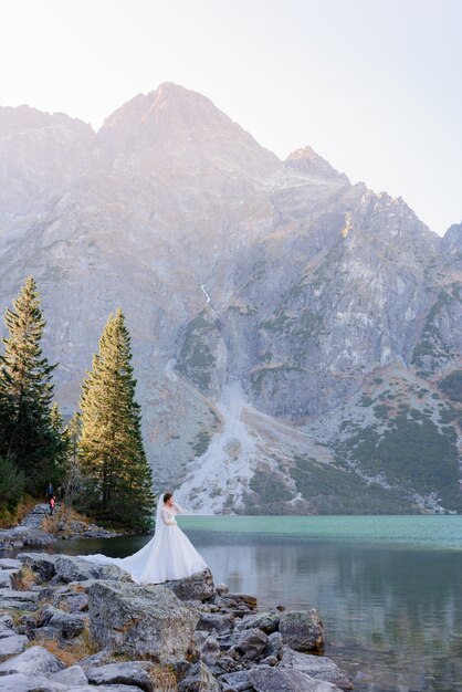 Vertical view of tiny bride in the mountains near the lake, standing on the rocks