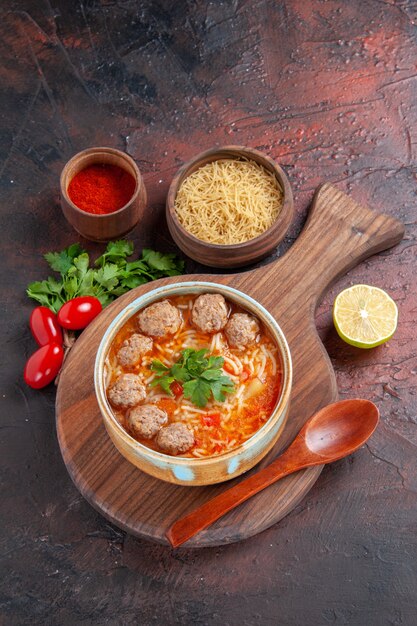 茶色のボウルに麺と暗い背景にさまざまなスパイスとトマトミートボールスープの垂直方向のビュー