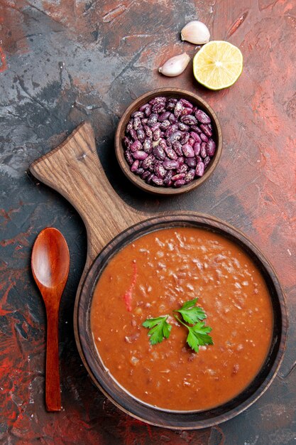 Vertical view of tomato soup beans and lemon on cutting board on a mixed color background