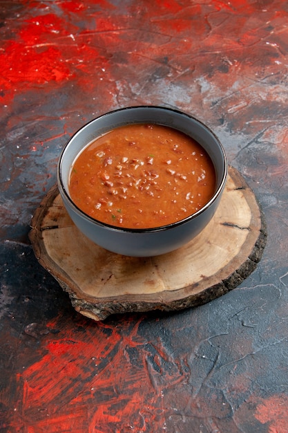 Foto gratuita vista verticale della zuppa di pomodoro in una ciotola blu su un vassoio di legno marrone sul tavolo di colori misti