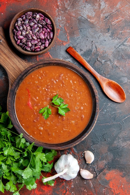 Vertical view of tomato soup on a brown cutting board on a mixed color background