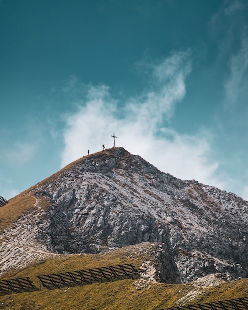 Vertical view of two people climbing near the cross on the top of a summit