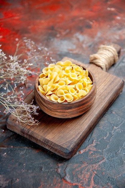 Vertical view of uncooked pastas on wooden cutting board on mixed color background
