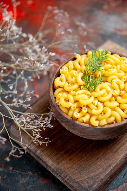 Vertical view of uncooked pastas on wooden cutting board on mixed color background