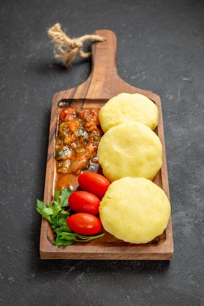 Vertical view of uncooked vegetables on brown cutting board on black