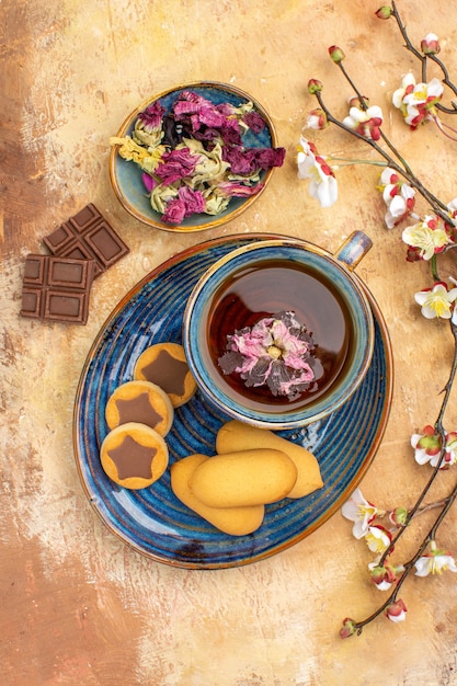 Foto gratuita vista verticale di vari biscotti una tazza di tè e fiori barrette di cioccolato sulla tabella di colori misti